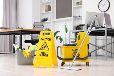 Photo of Cleaning service. Mop, wet floor sign and bucket with supplies in office