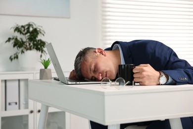 Photo of Man with cup of drink sleeping at table in office