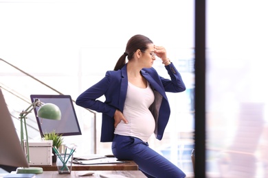 Photo of Young pregnant woman suffering from pain while working in office