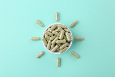 Bowl with vitamin capsules on turquoise background, top view
