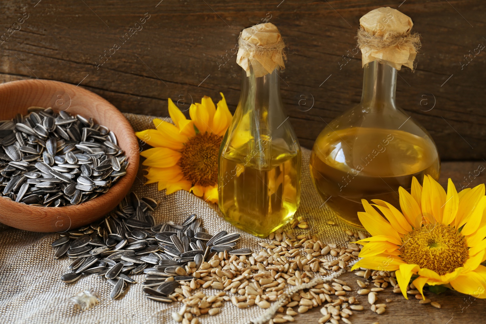 Photo of Bottles of sunflower oil, seeds and flowers on wooden table