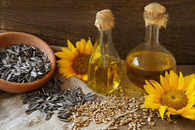 Bottles of sunflower oil, seeds and flowers on wooden table