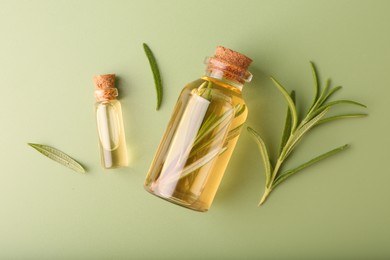 Aromatic essential oils in bottles and rosemary on green background, flat lay