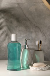 Photo of Bottle of mouthwash, toothbrushes and soap on light table in bathroom