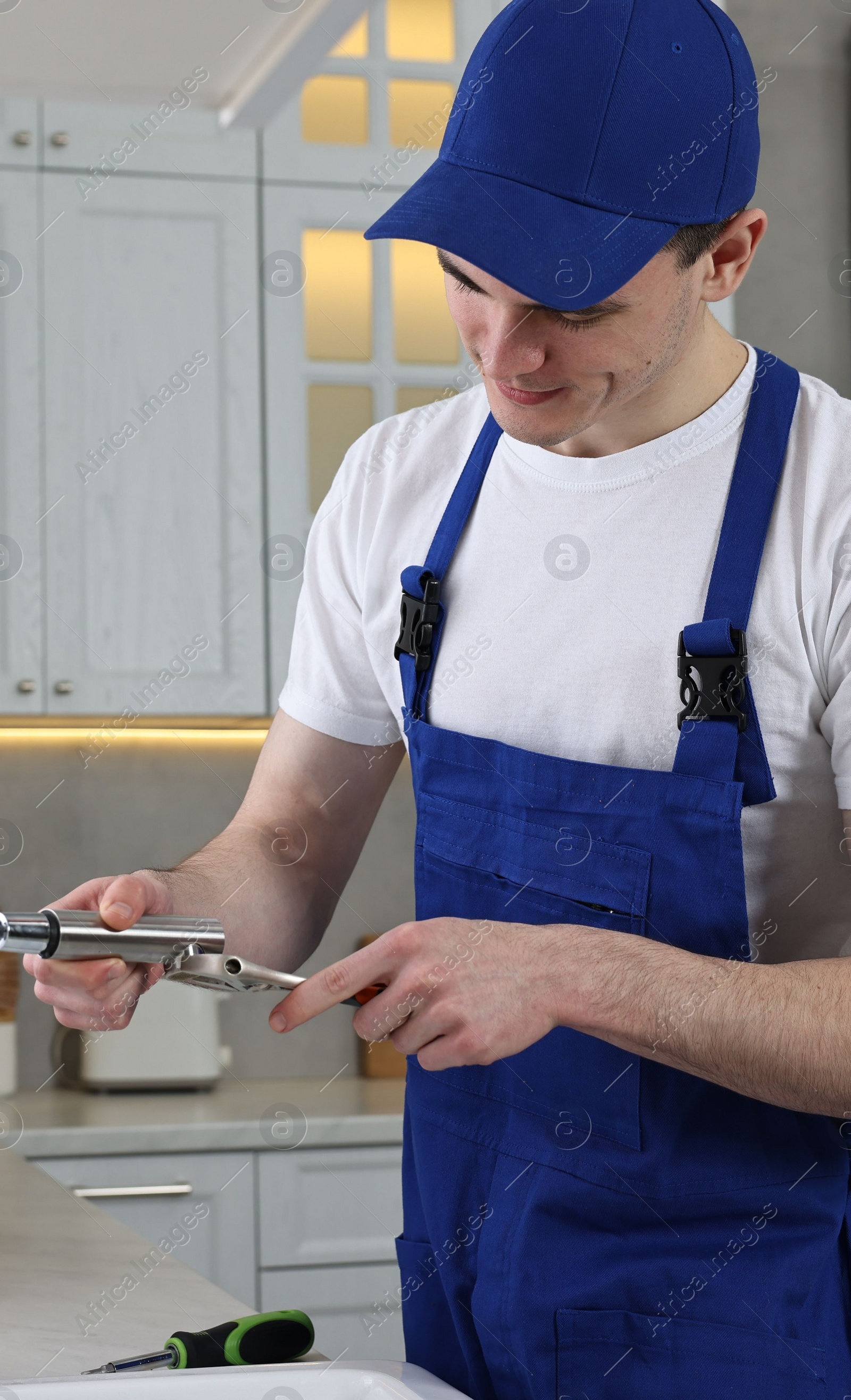 Photo of Young plumber repairing faucet with spanner in kitchen