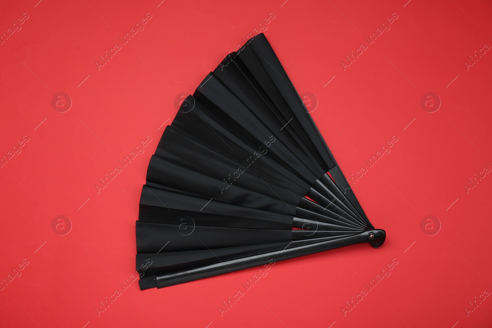 Photo of Stylish black hand fan on red background, top view