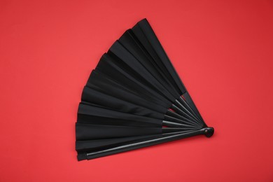 Photo of Stylish black hand fan on red background, top view