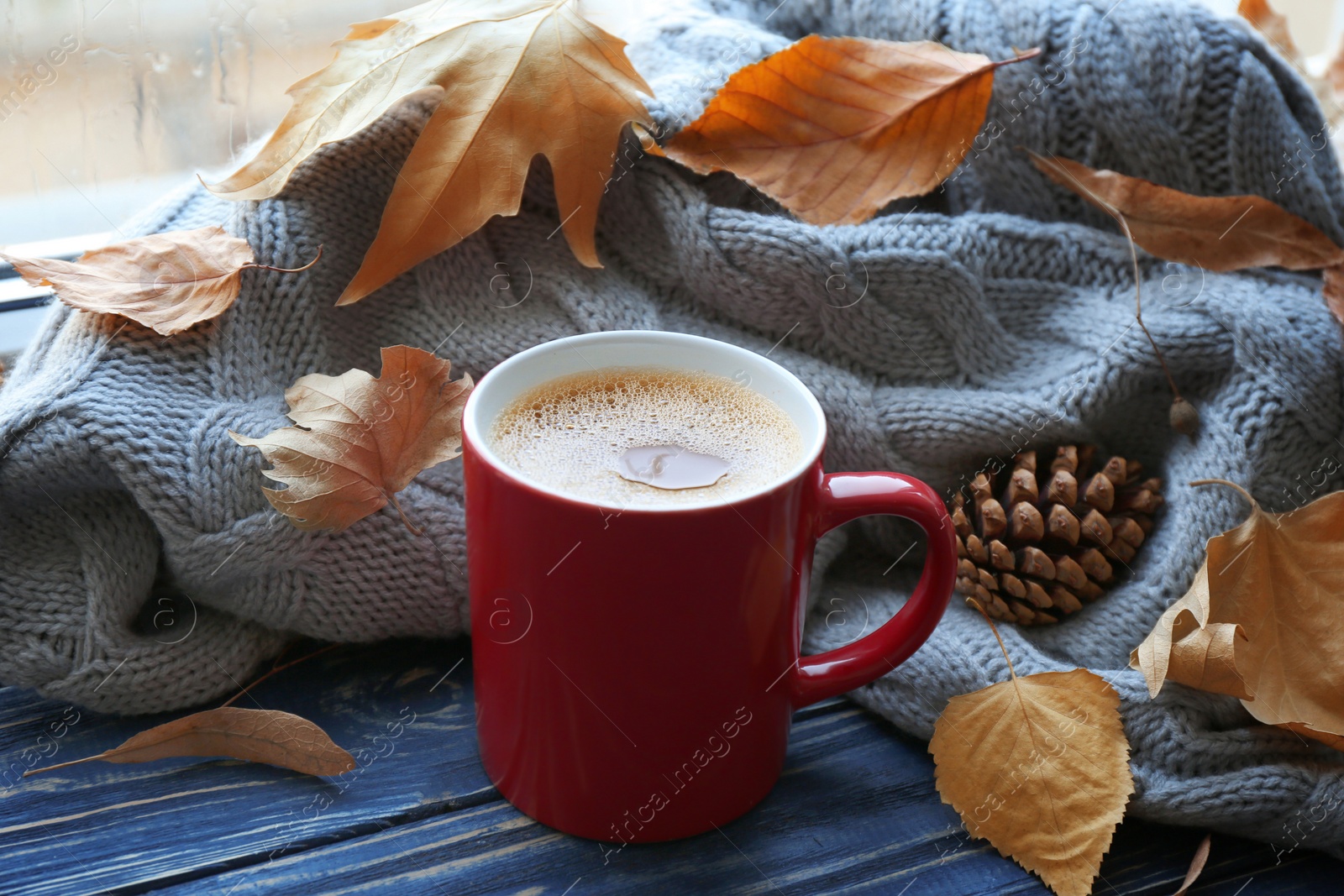 Photo of Cup of hot drink, sweater and autumn leaves on windowsill. Cozy atmosphere