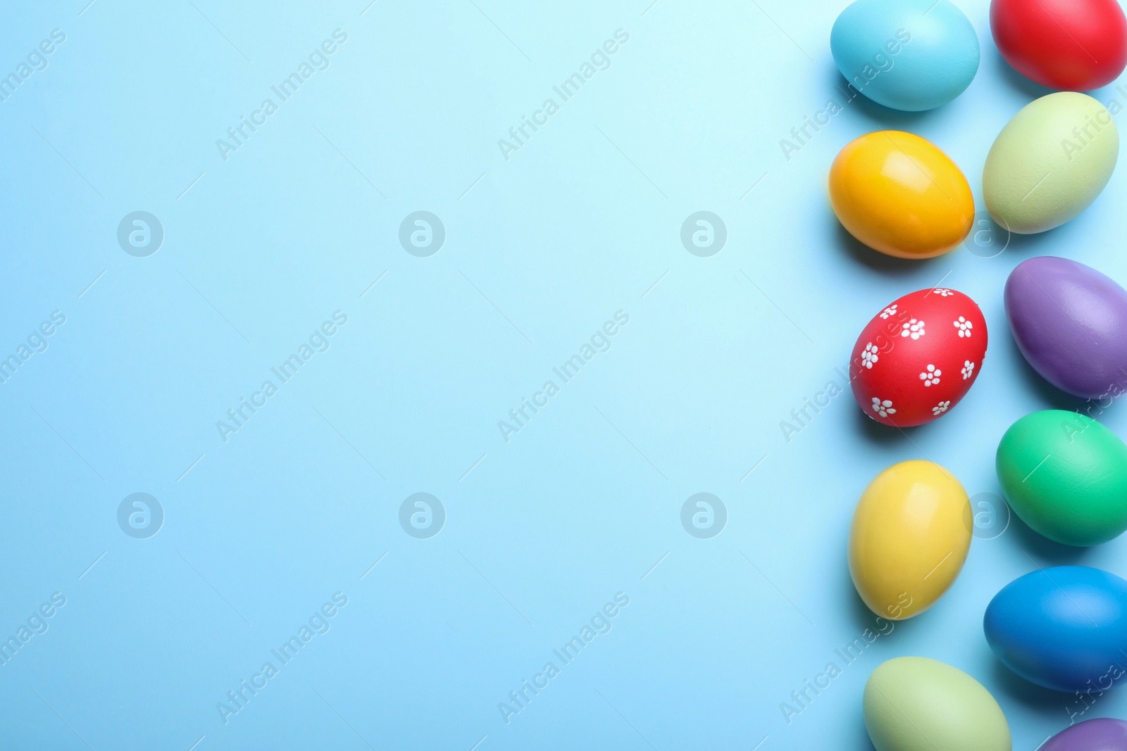 Photo of Bright painted eggs on light blue background, flat lay with space for text. Happy Easter