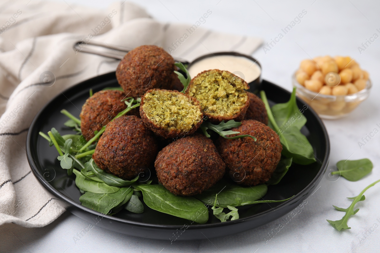 Photo of Delicious falafel balls, herbs, chickpeas and sauce on white marble table