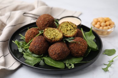 Photo of Delicious falafel balls, herbs, chickpeas and sauce on white marble table