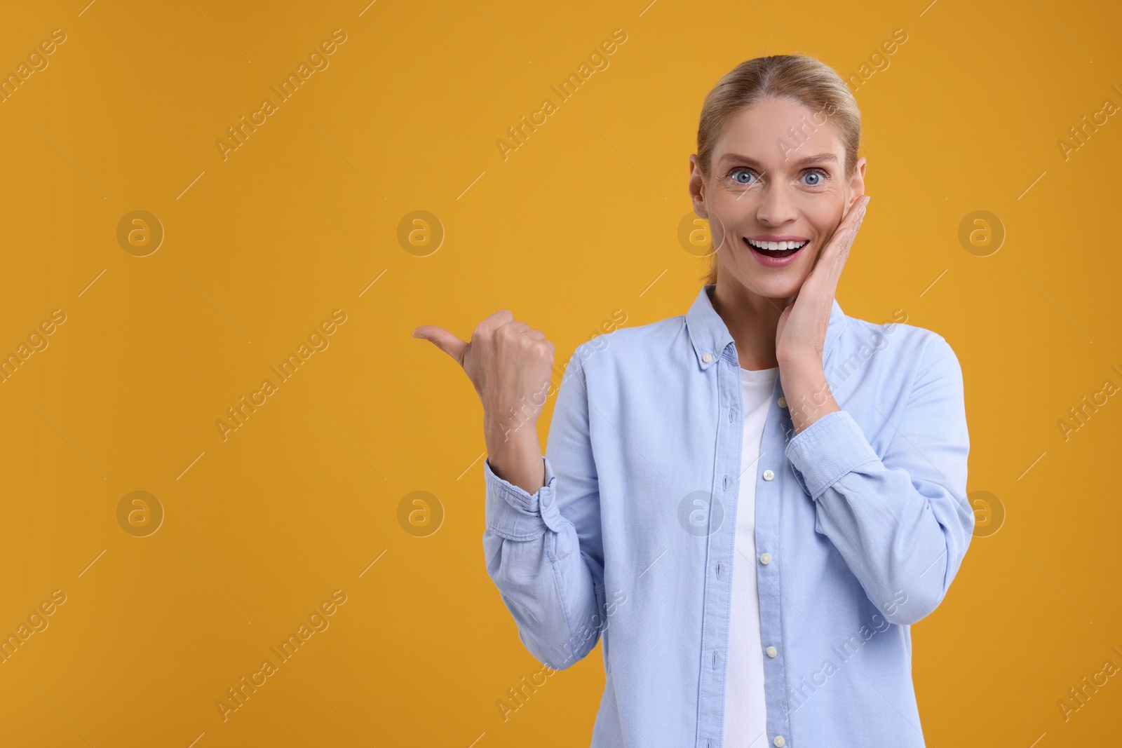 Photo of Special promotion. Smiling woman pointing at something on orange background. Space for text