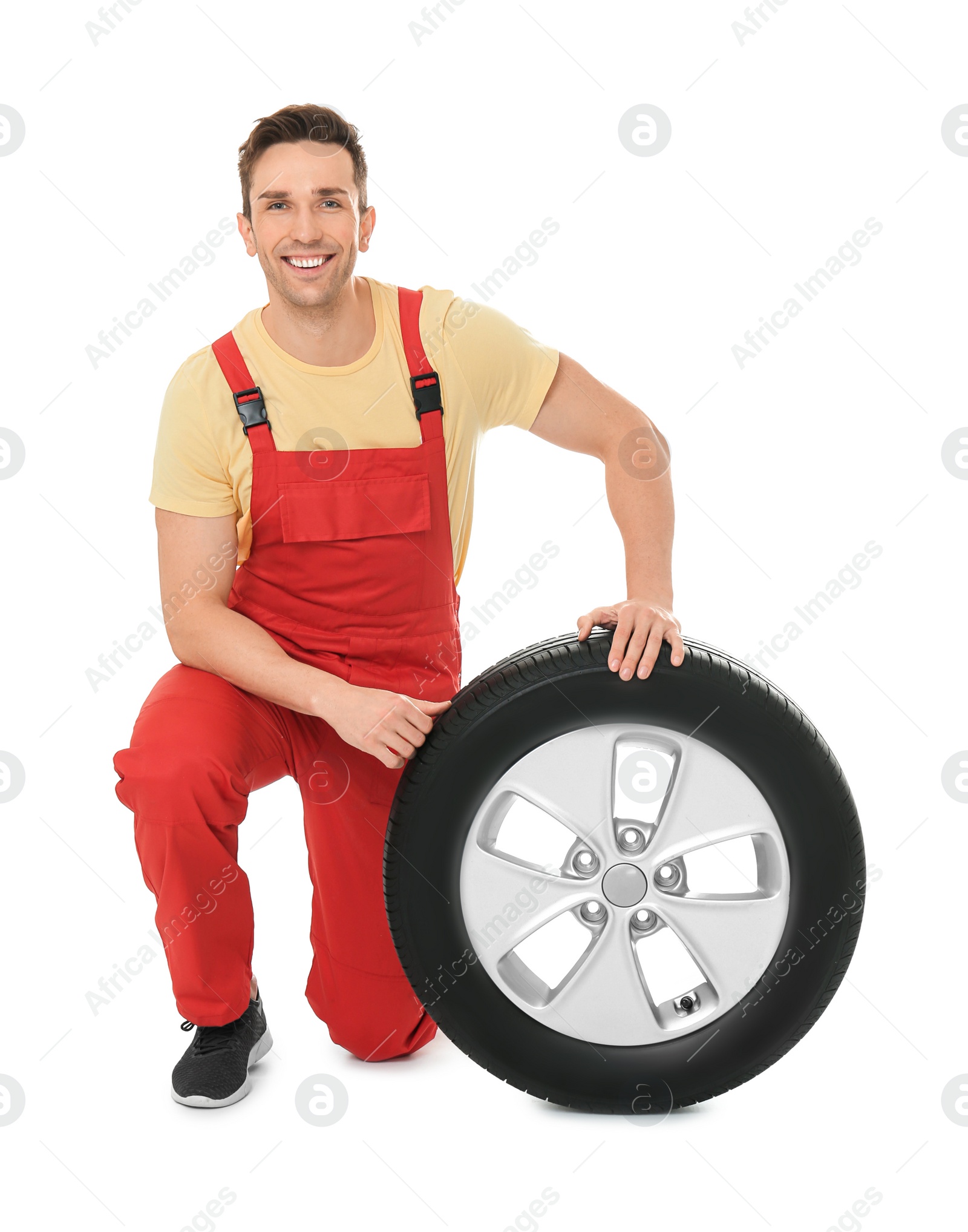 Photo of Young mechanic in uniform with car tire on white background