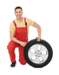 Young mechanic in uniform with car tire on white background