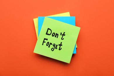 Paper note with phrase Don't Forget on orange background, top view
