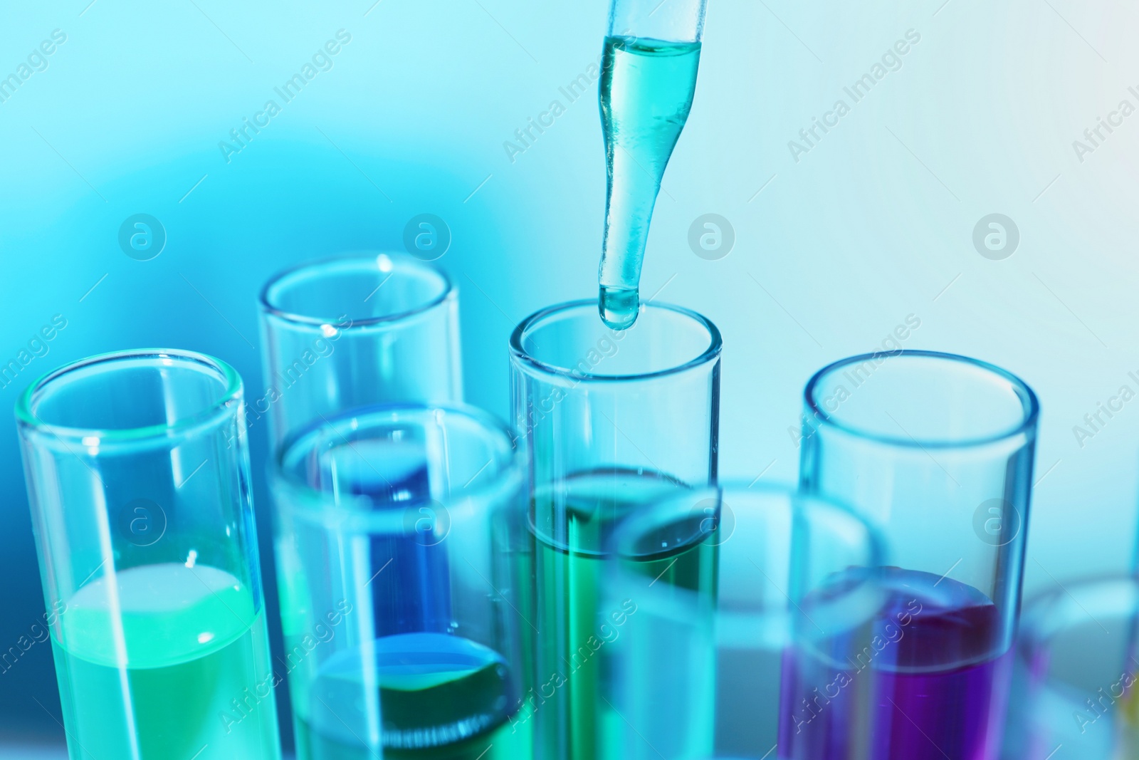 Photo of Dripping liquid from pipette into test tube on blurred background, closeup