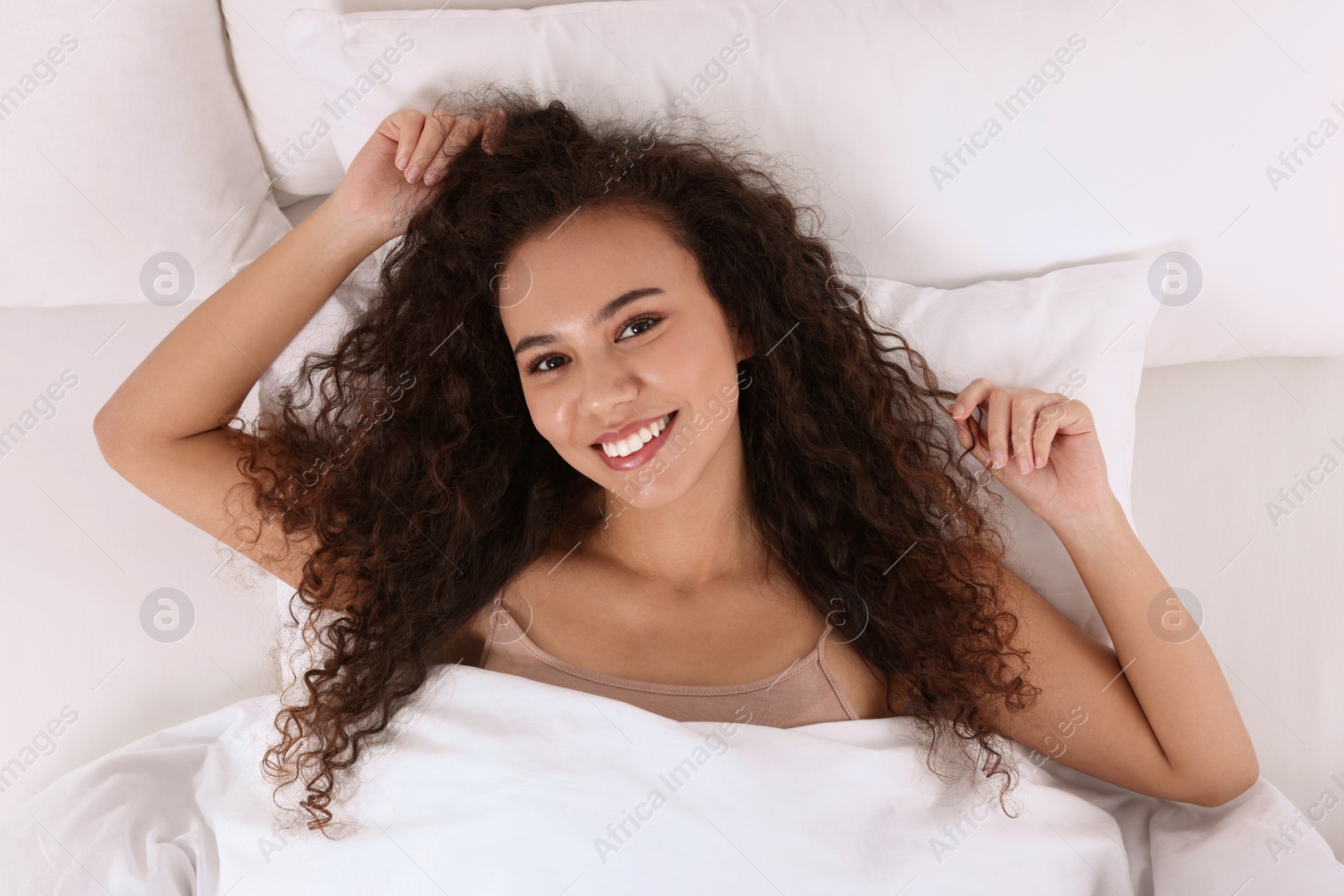 Photo of Happy African American woman awakening in bed, top view