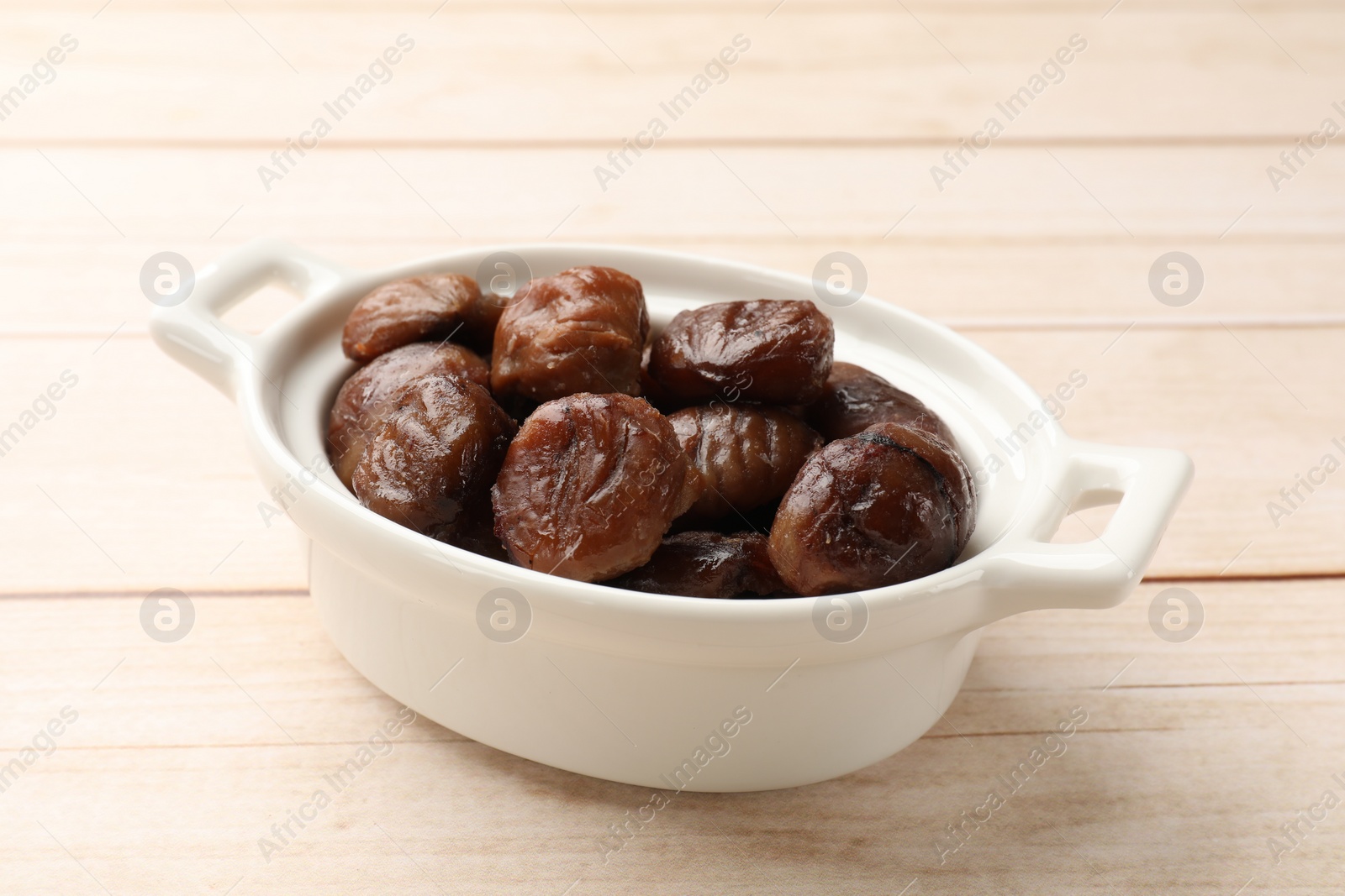 Photo of Roasted edible sweet chestnuts in dish on light wooden table