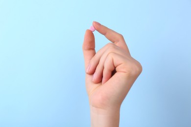 Woman holding vitamin pill on light blue background, closeup