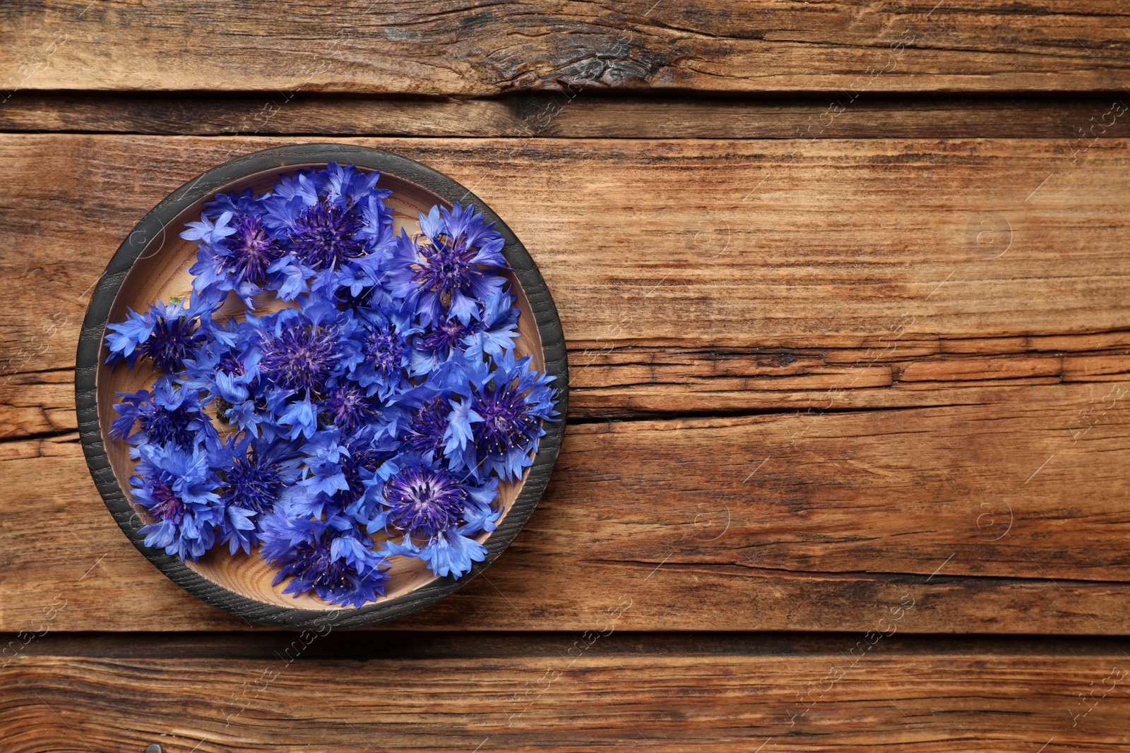 Photo of Beautiful blue cornflowers in bowl on wooden table, top view. Space for text
