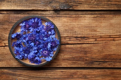 Beautiful blue cornflowers in bowl on wooden table, top view. Space for text