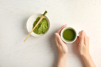 Woman with cup of matcha tea at table, top view