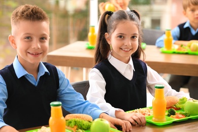 Photo of Happy children at table with healthy food in school canteen