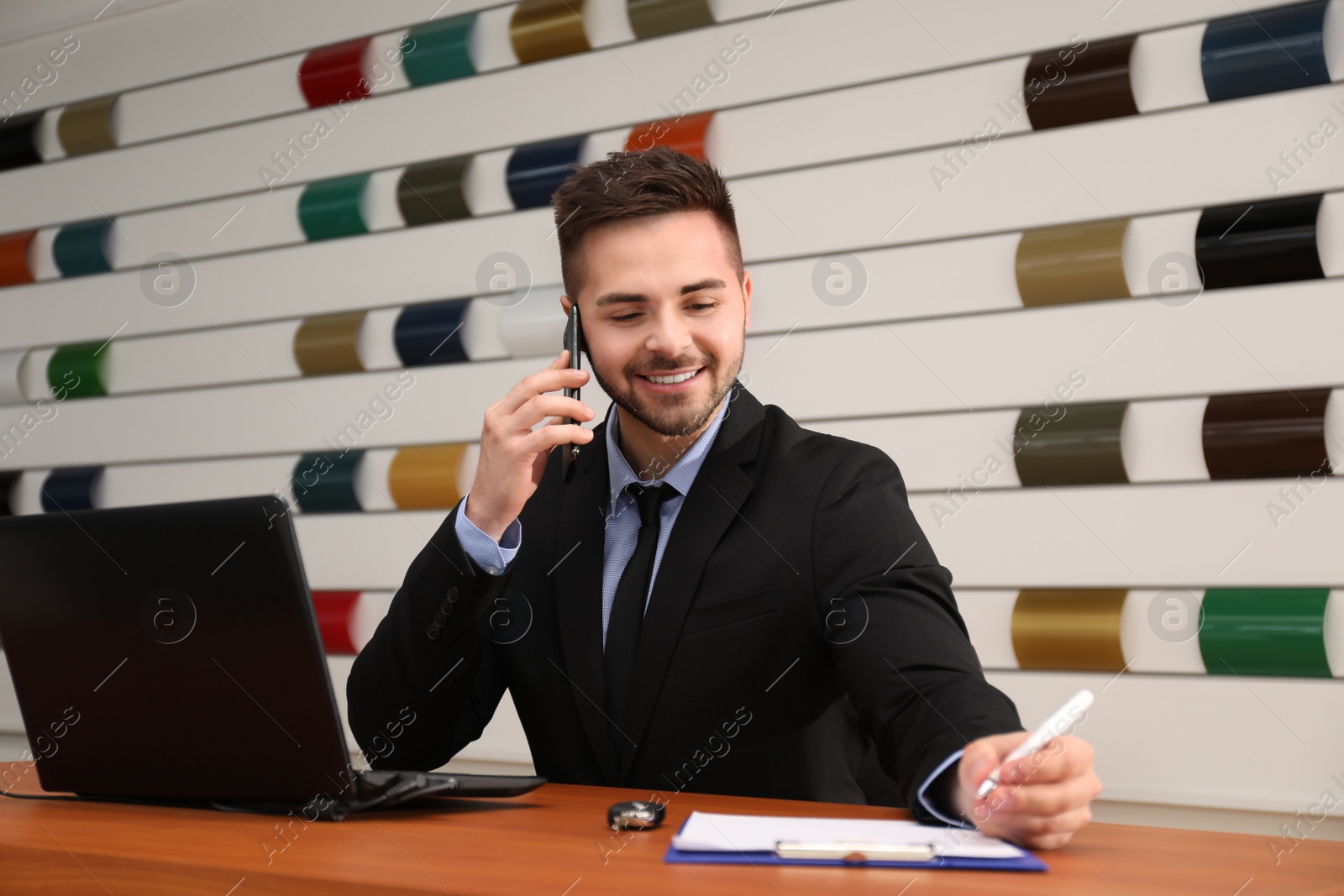 Photo of Salesman talking on phone at desk in car dealership
