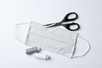 Homemade protective mask, threads and scissors on white background, flat lay. Sewing idea