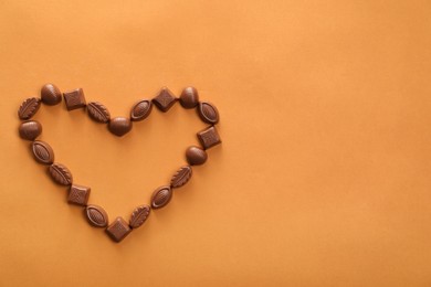 Heart made with delicious chocolate candies on brown background, top view. Space for text