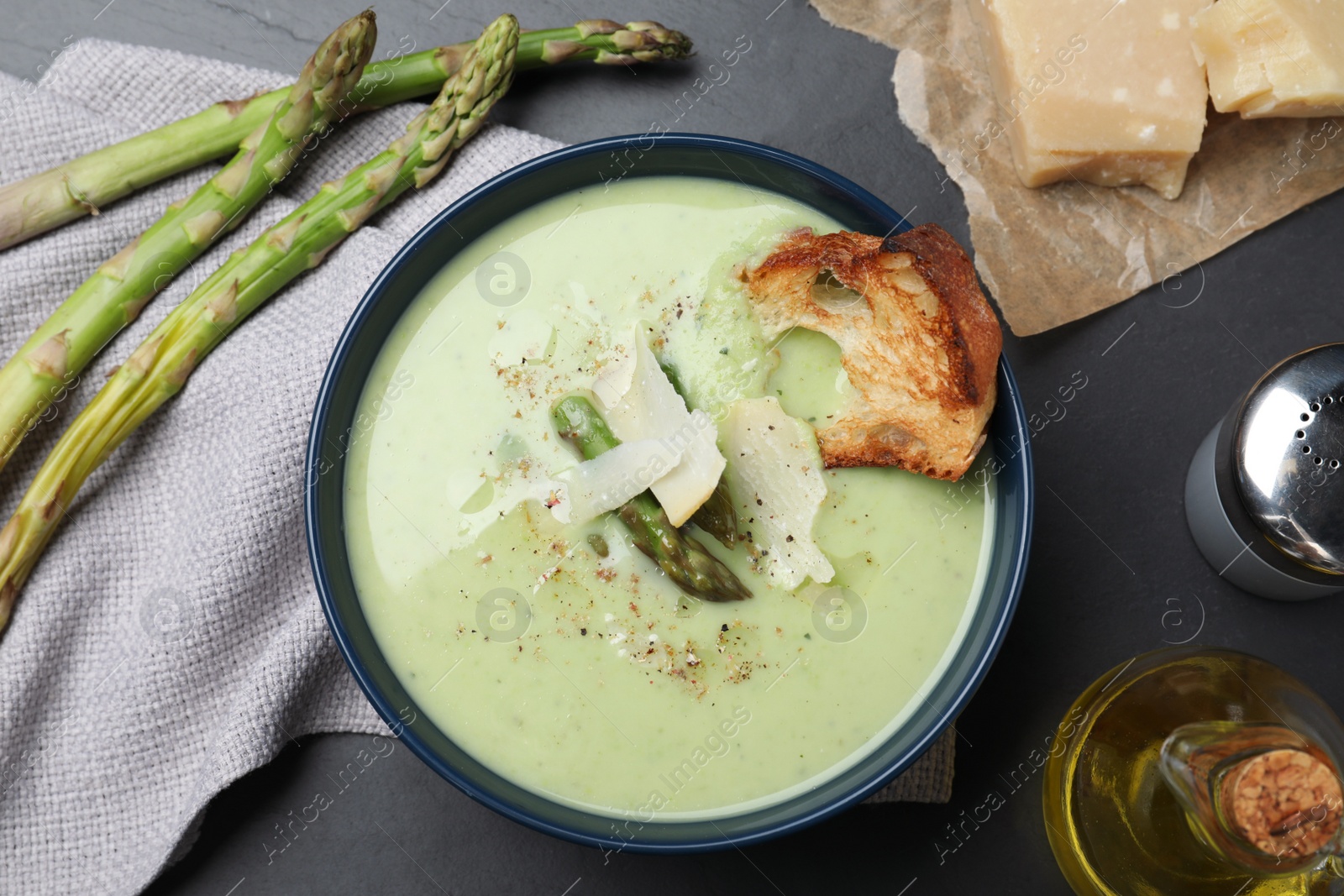 Photo of Bowl of delicious asparagus soup served on dark table, flat lay