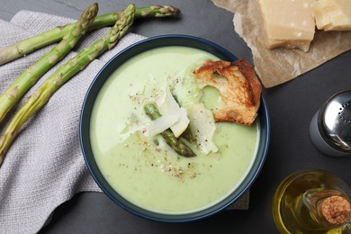 Photo of Bowl of delicious asparagus soup served on dark table, flat lay