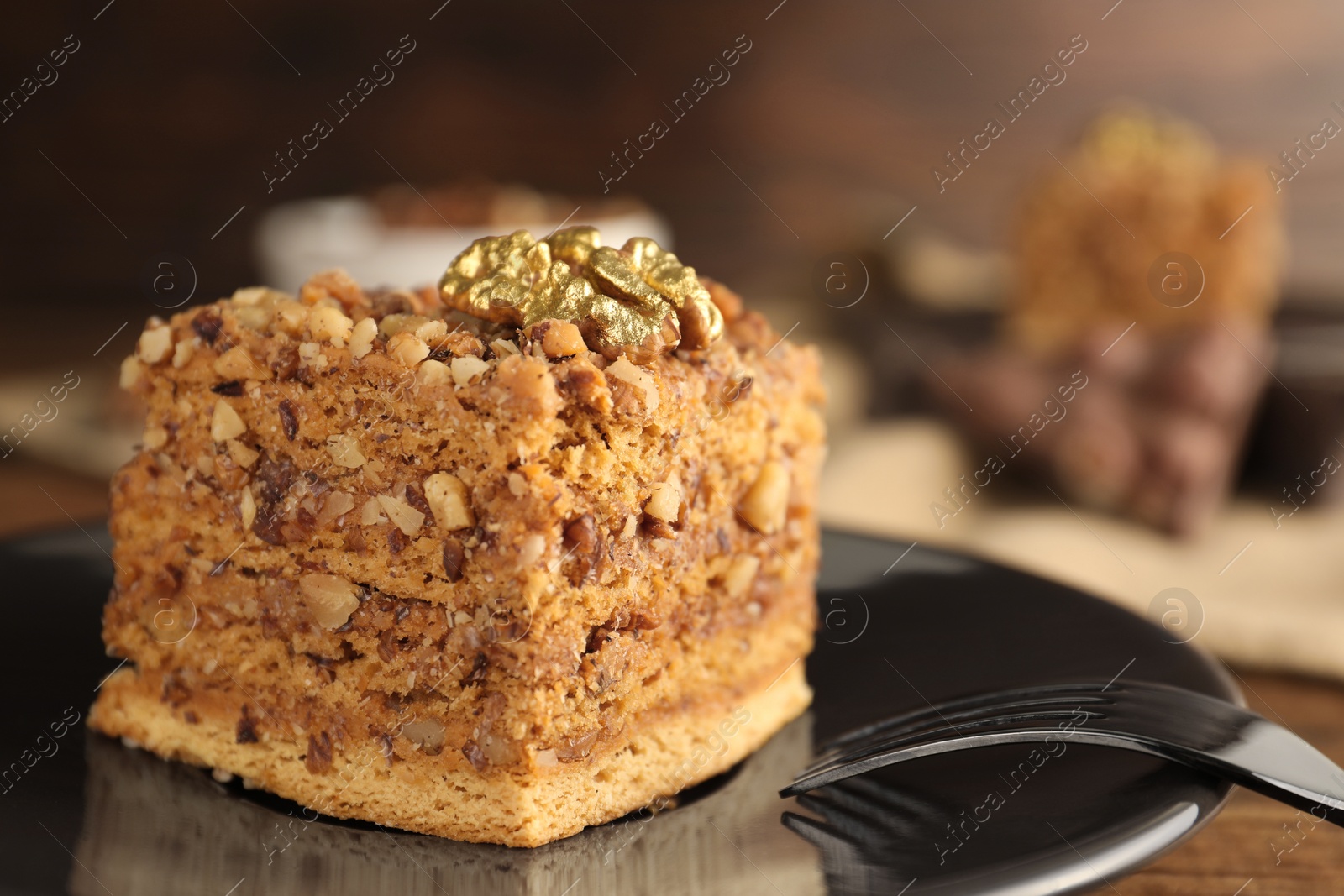 Photo of Piece of honey cake with walnuts and fork on plate, closeup