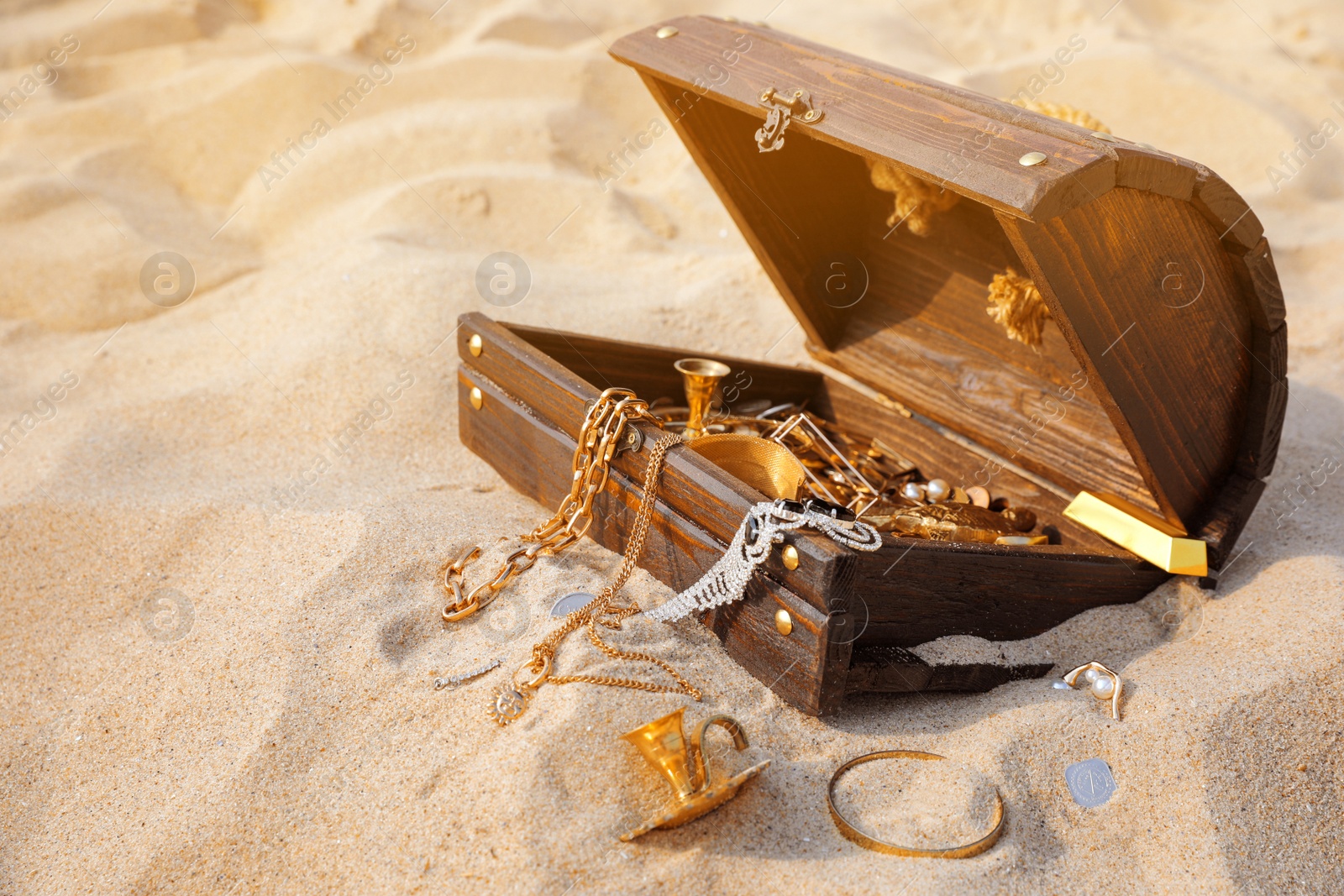 Photo of Open wooden treasure chest on sand, space for text