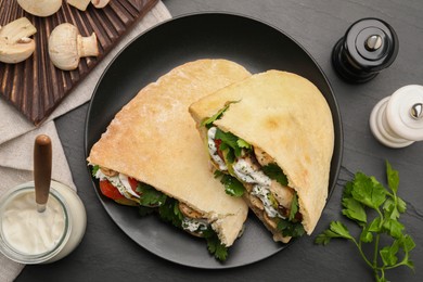 Photo of Delicious pita sandwiches with grilled vegetables and sour cream sauce on black textured table, flat lay