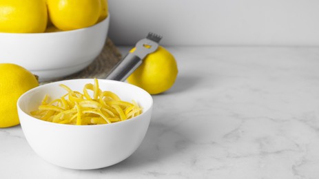 Photo of Bowl with peel pieces, fresh lemons and zester on white marble table. Space for text