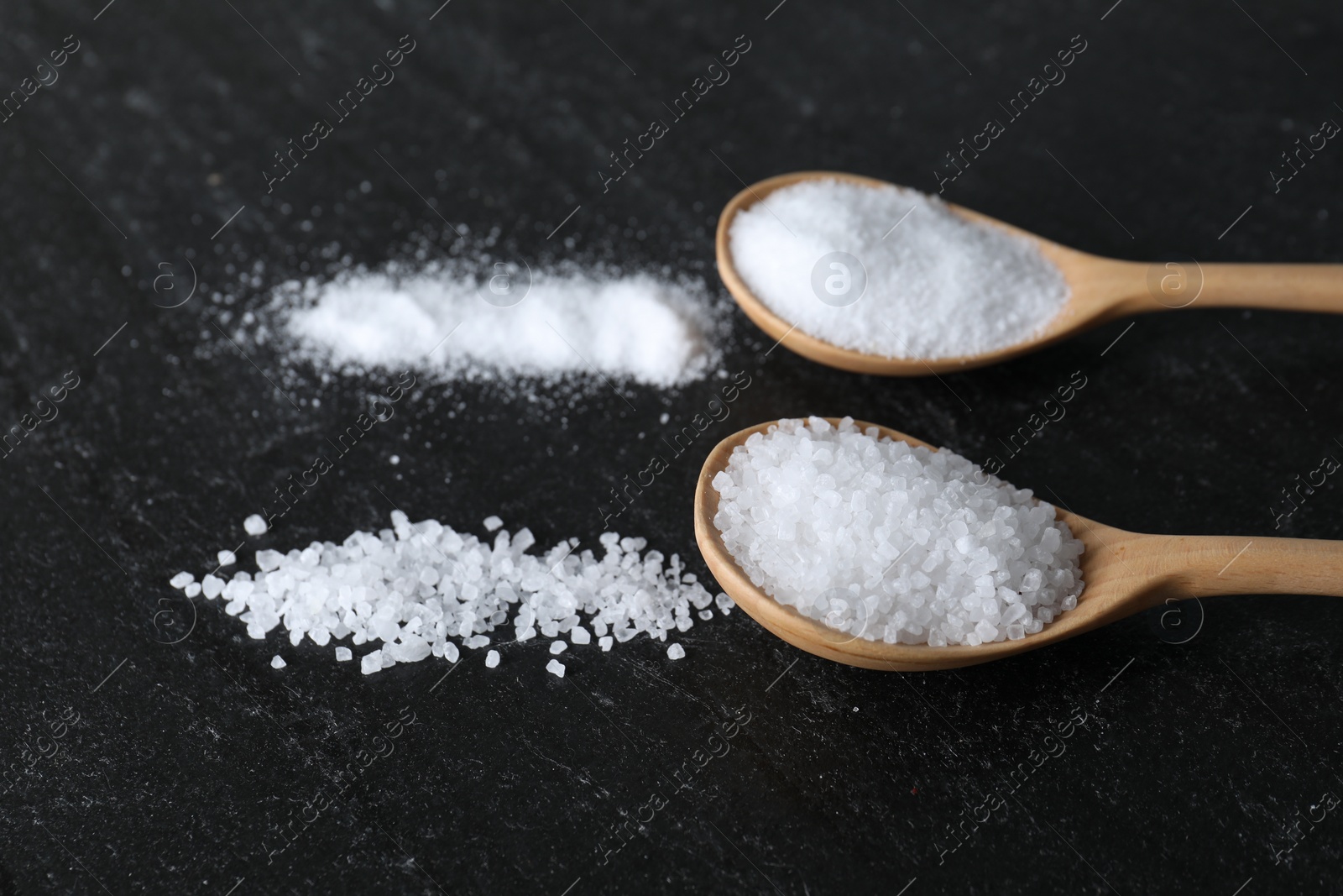 Photo of Organic salt in spoons on black table, closeup