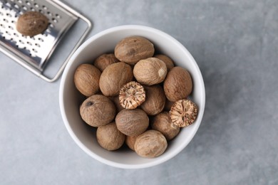 Photo of Nutmegs in bowl and metal grater on light grey table, flat lay