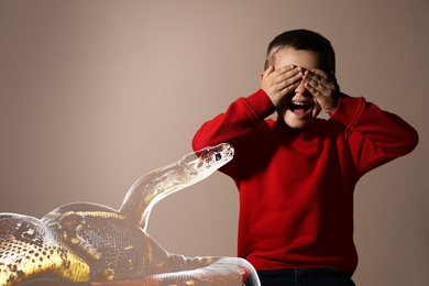 Image of Double exposure of scared little boy suffering from herpetophobia on beige background. Fear or aversion to reptiles
