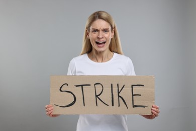 Photo of Angry woman holding cardboard banner with word Strike on grey background