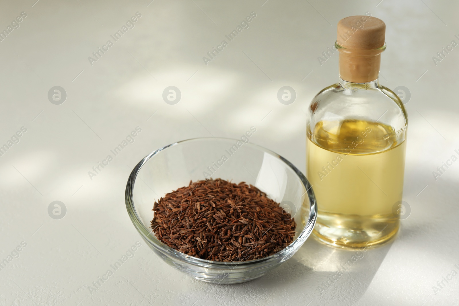 Photo of Caraway (Persian cumin) seeds in bowl and essential oil on white table