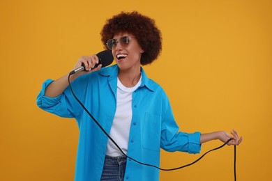 Photo of Curly young woman in sunglasses with microphone singing on yellow background
