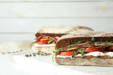 Delicious sandwiches with fresh vegetables and prosciutto on white table