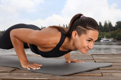 Photo of Young woman doing plank exercise on wooden pier near river