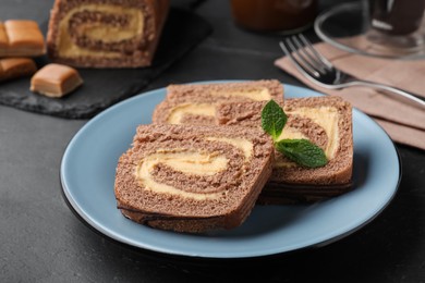 Photo of Tasty chocolate cake roll with cream on black table, closeup