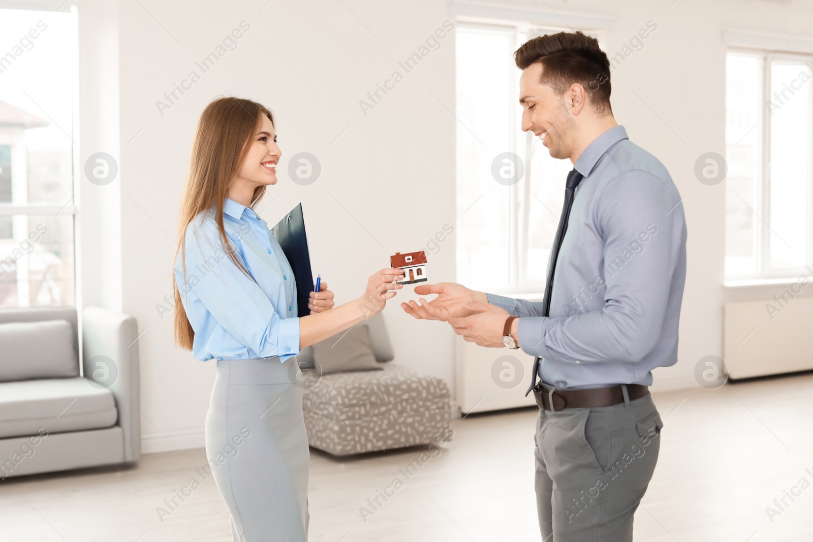 Photo of Beautiful real estate agent giving house model to young man indoors