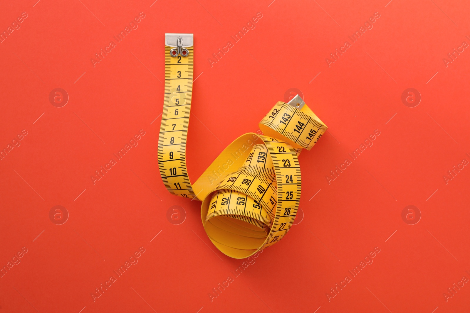 Photo of Yellow measuring tape on orange background, top view