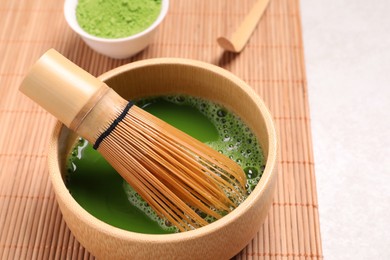 Photo of Bowl of fresh matcha tea with bamboo whisk and powder on light table, closeup. Space for text