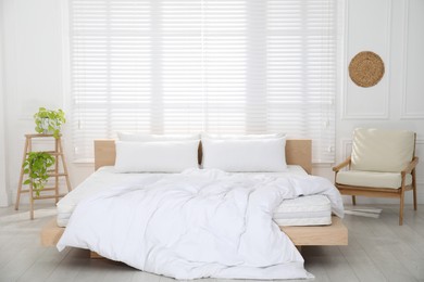 Wooden bed with soft white mattress, blanket and pillows in cozy room interior