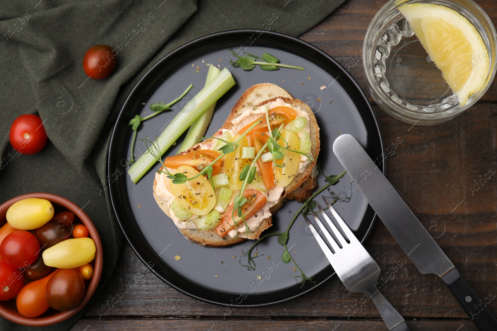 Photo of Tasty vegan sandwich with tomatoes, celery, microgreens, fork and knife on wooden table, flat lay